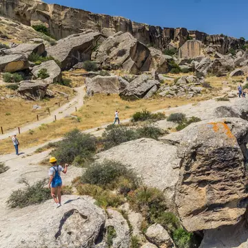  Tourists visit Gobustan petroglyph reserve, Azerbaijan. Overhead rock formations and blue sky.