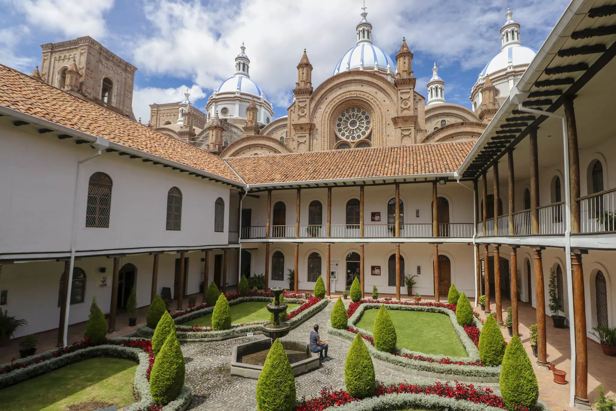 A person sits in the very neat gardens within a courtyard of a large cathedral