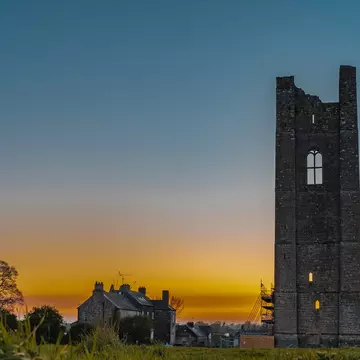 A golden yellow sunset with a stone tower, stone house, and leafless tree in the foreground.