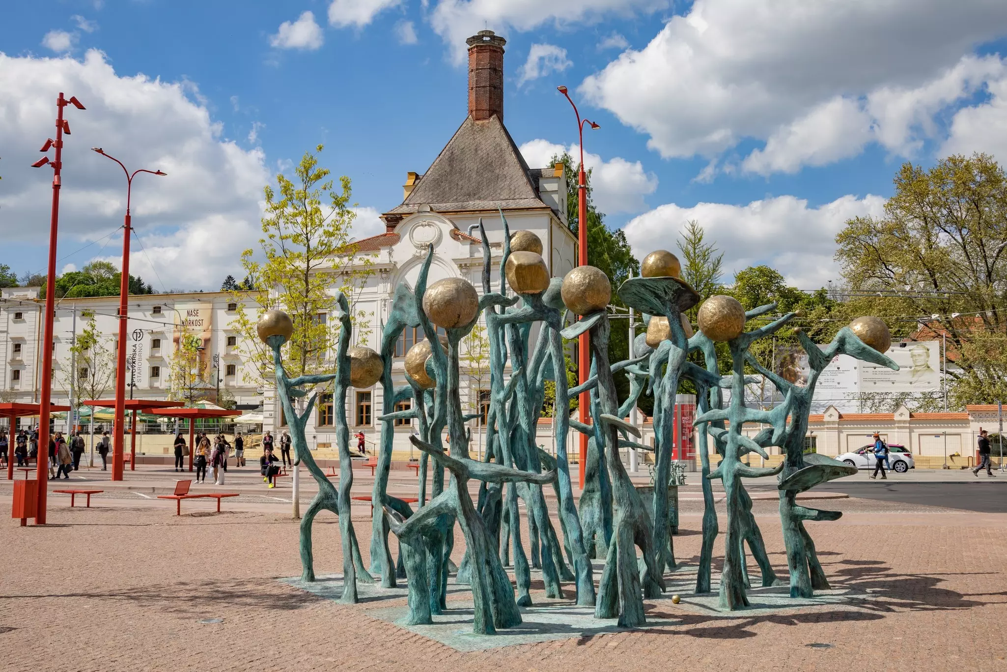 A sculpture of metal strips and orbs resembling pea plants is displayed in the square of a city.