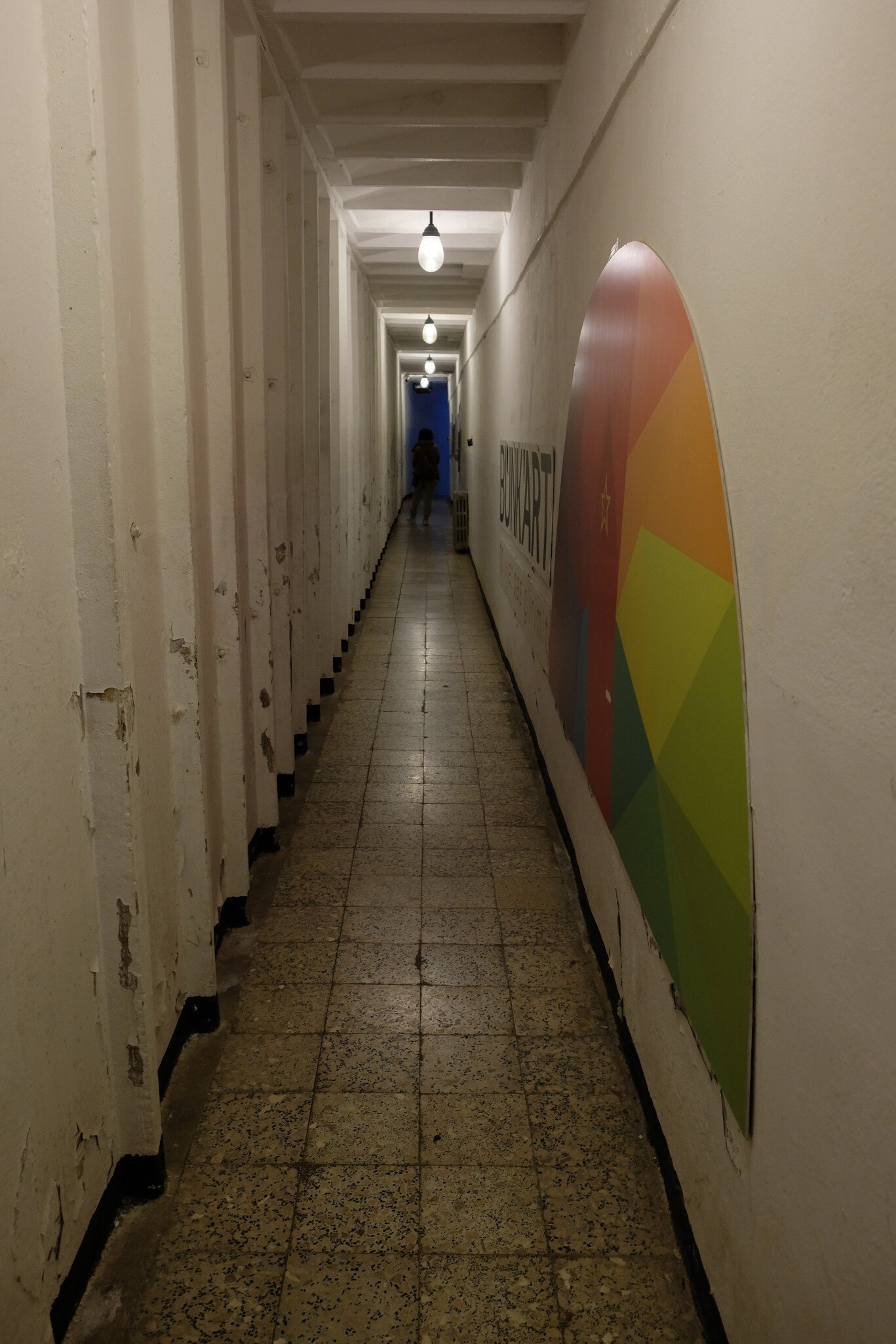 Dim concrete bunker corridor lined with heavy doors, a colourful painted BUNK'ART sign on the right-hand wall.