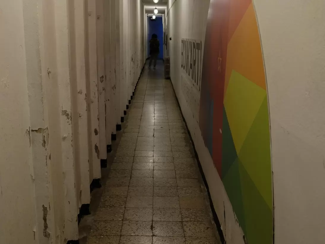 Dim concrete bunker corridor lined with heavy doors, a colourful painted BUNK'ART sign on the right-hand wall.