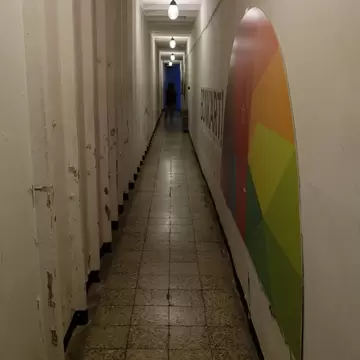 Dim concrete bunker corridor lined with heavy doors, a colourful painted BUNK'ART sign on the right-hand wall.