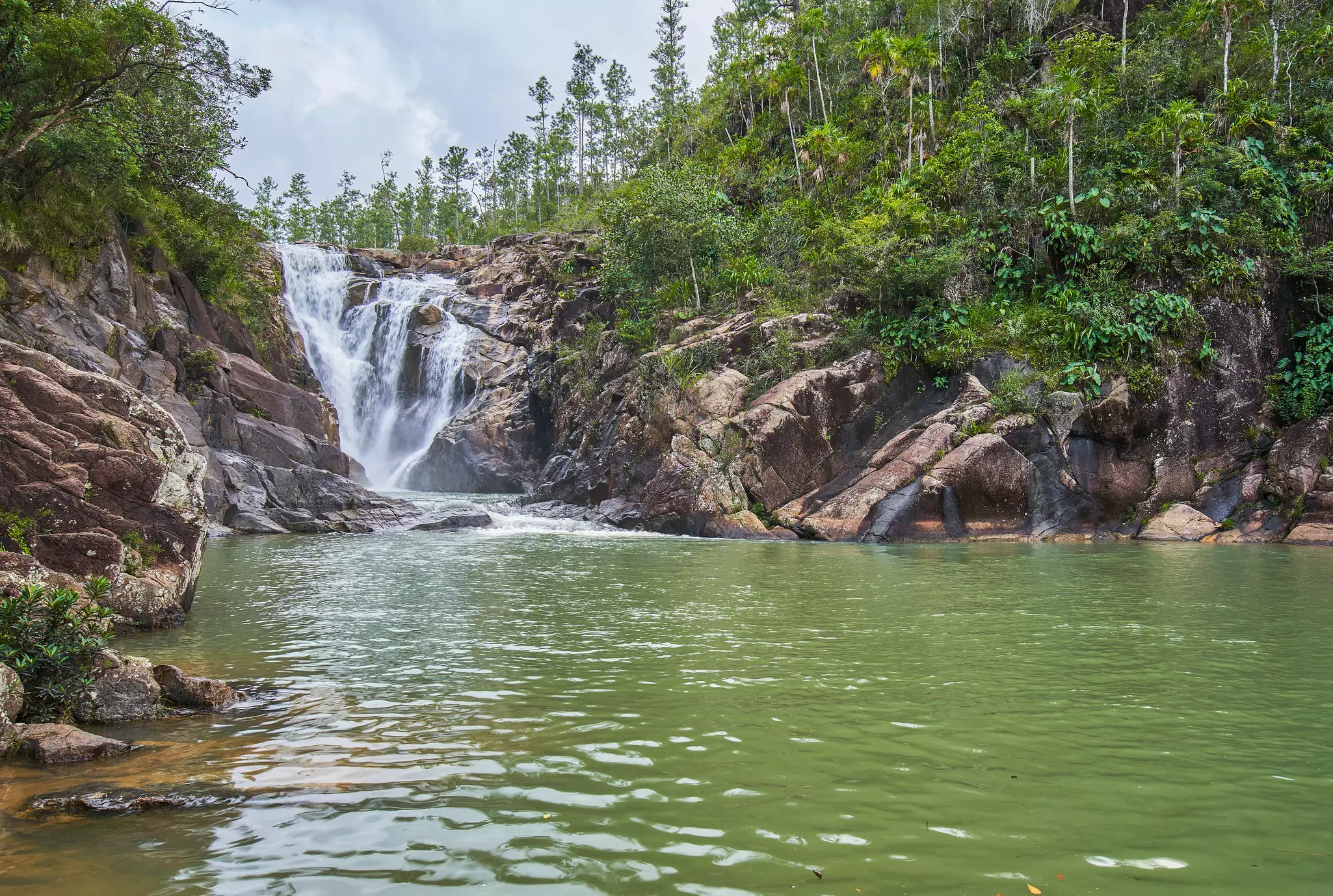 A waterfall plunges into a pool surrounded by big boulders.