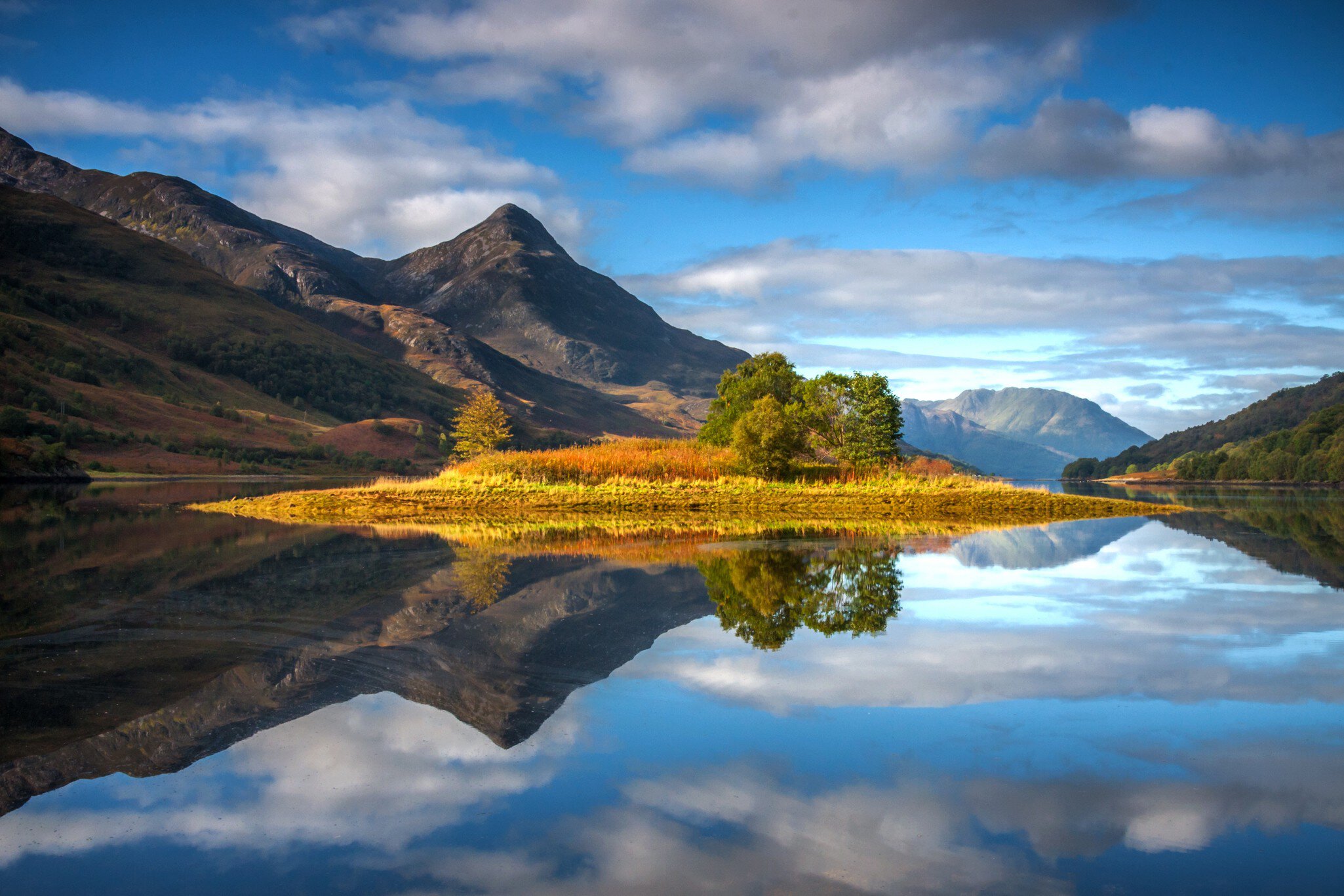Reflections of the island in Loch Leven, Scotland, with the Pap of Glencoe in the middle distance.