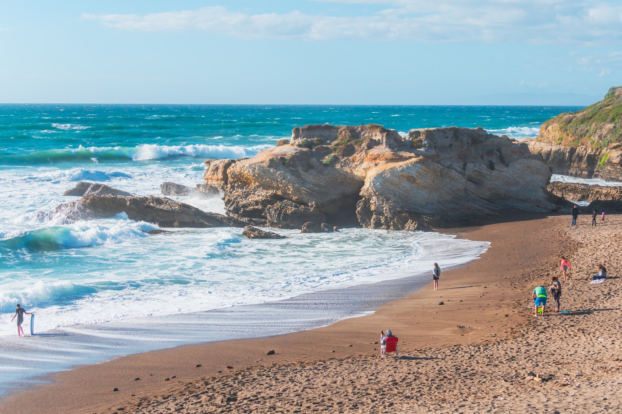 Rocky cliffs, sandy beach, and people enjoying beautiful sunny day at Montana de Oro State Park, California.