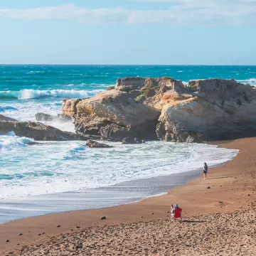 Rocky cliffs, sandy beach, and people enjoying beautiful sunny day at Montana de Oro State Park, California.