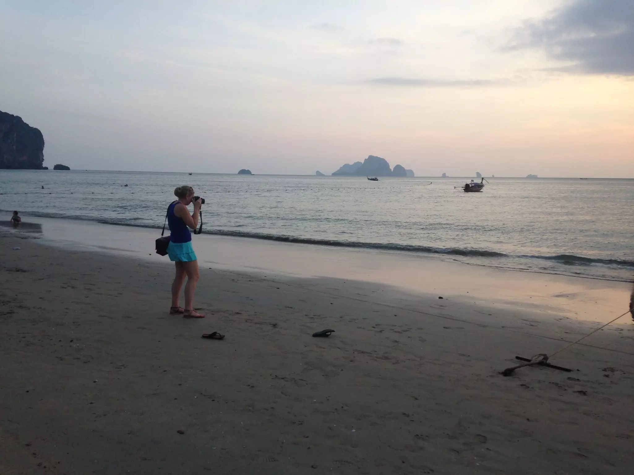 A woman stands on a beach taking a photo of the ocean with a DSLR camera.