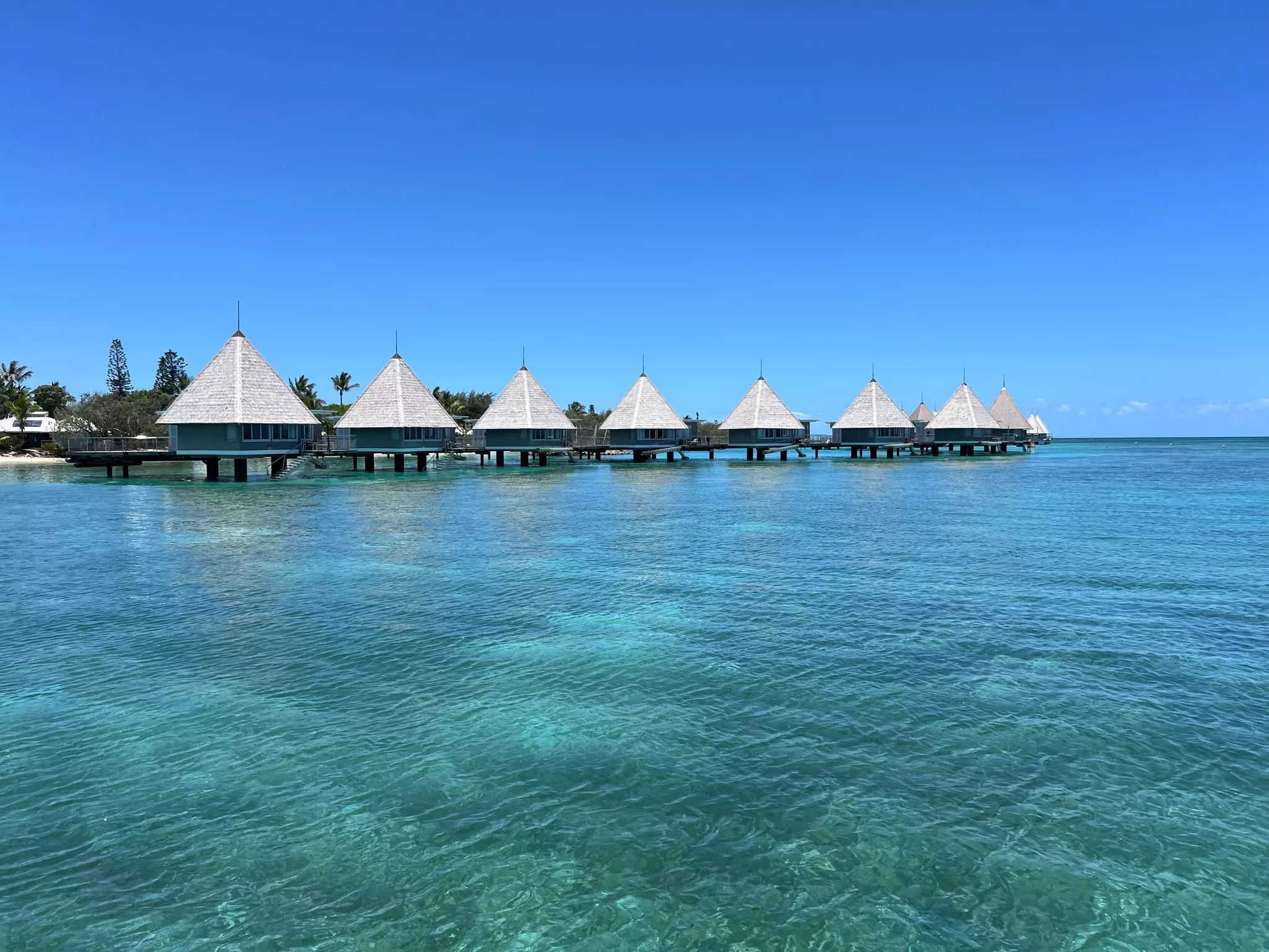 A row of thatched bungalows built out on a boardwalk over the ocean.