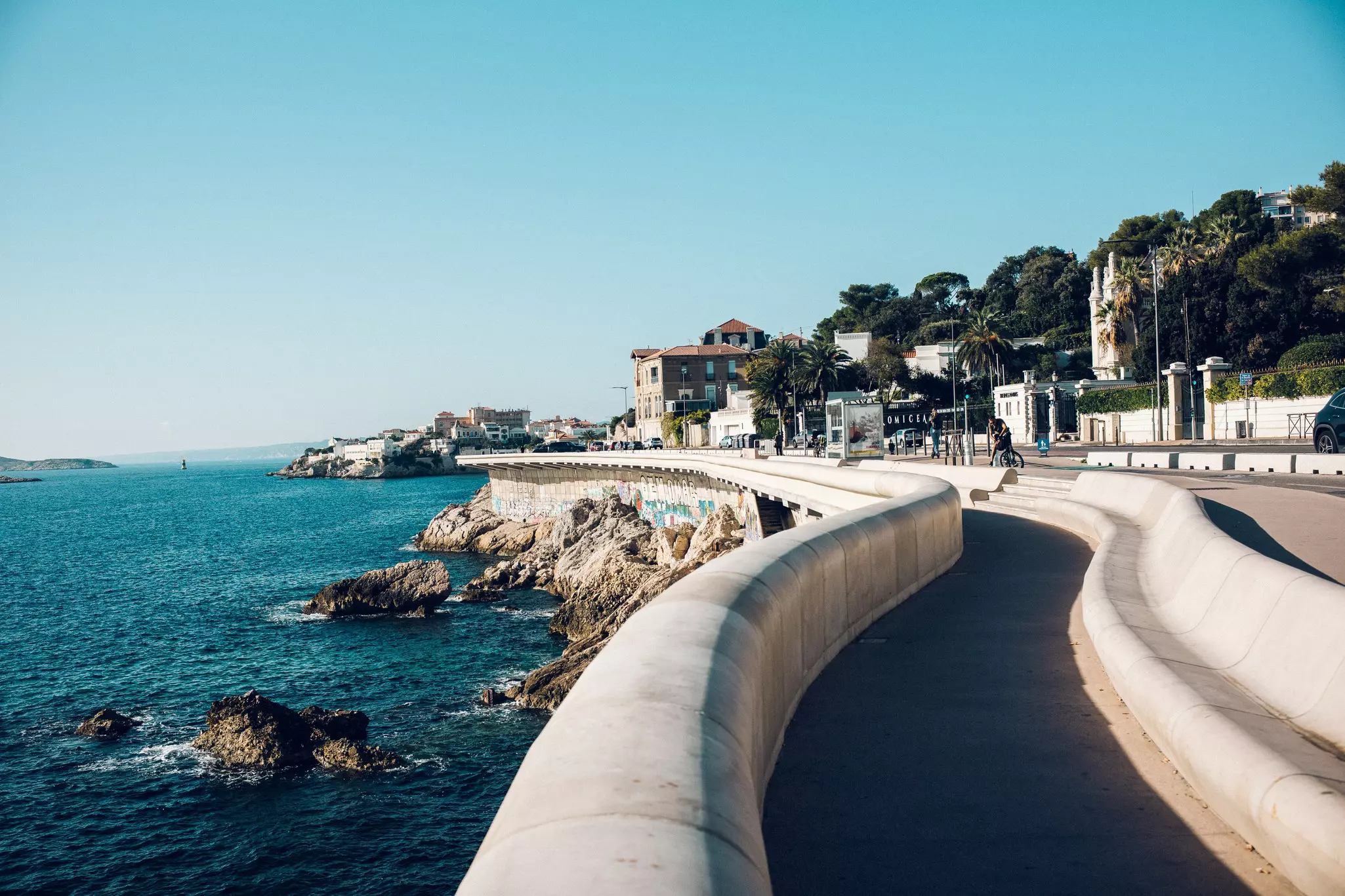 A paved bike path winds directly along the shore of the sea in a city.