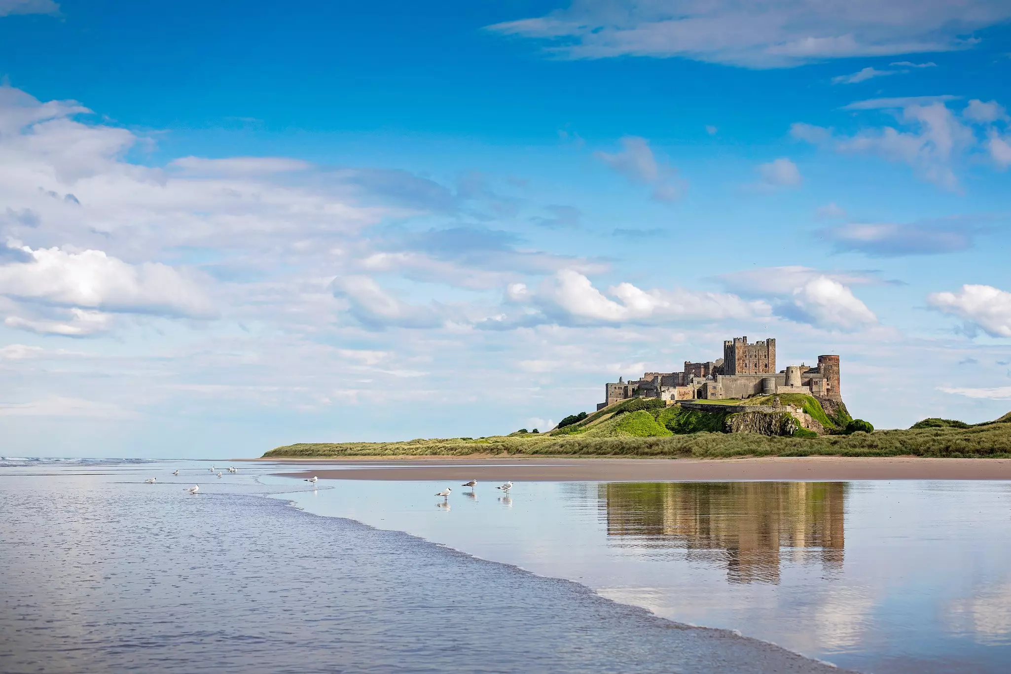 A wide stretch of wet beach overlooked by a vast clifftop fortress