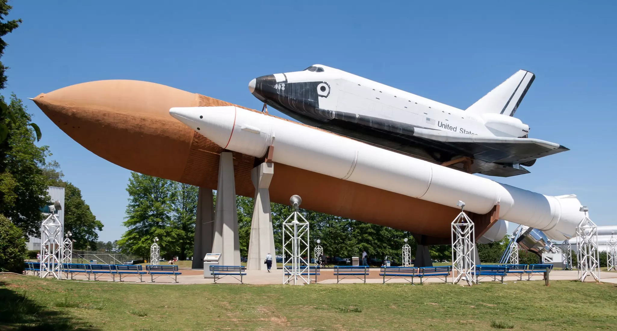 Space shuttle attached to a rocket outside a museum on a sunny afternoon.