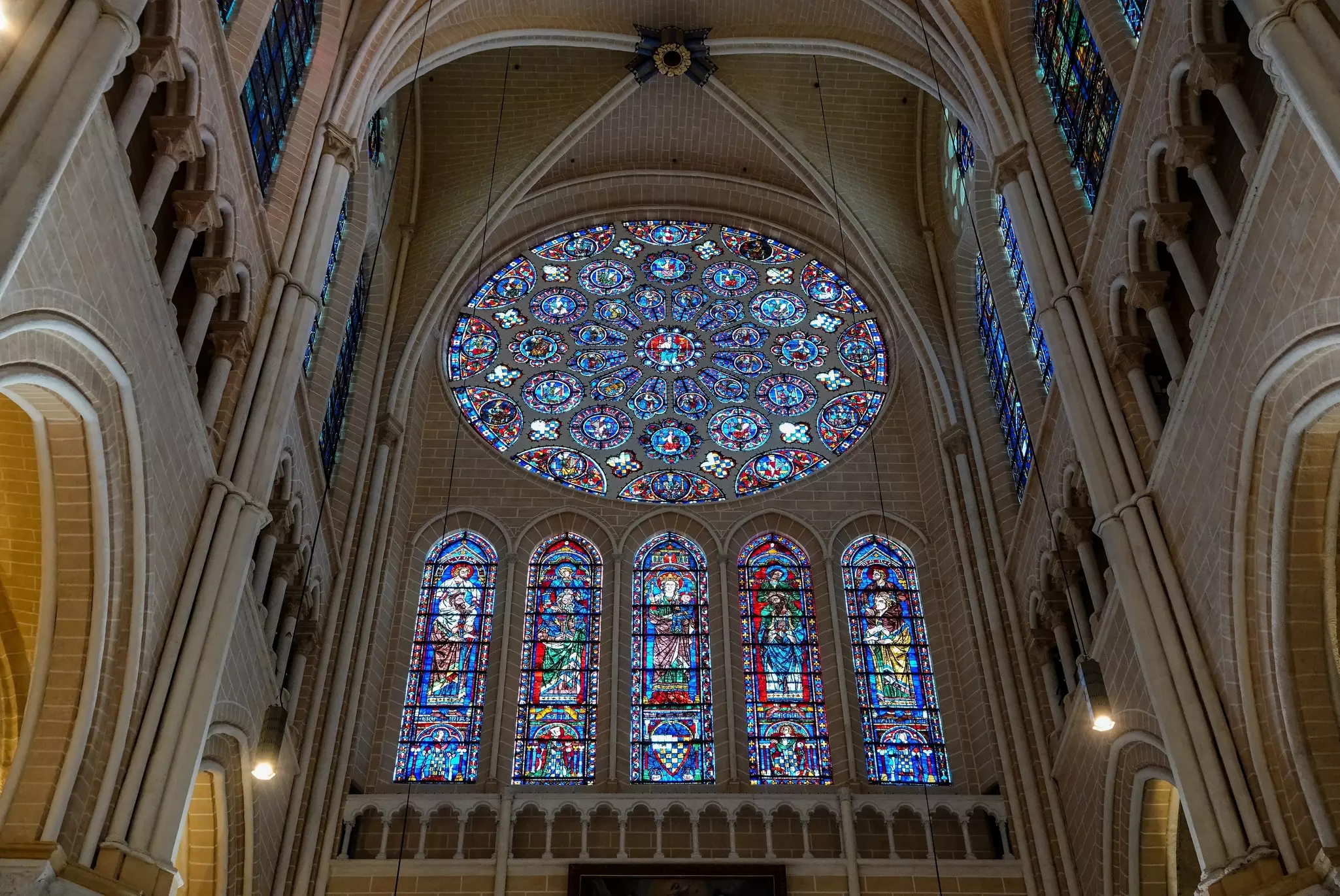 A large round stained glass window, with five long stained glass panels below it.