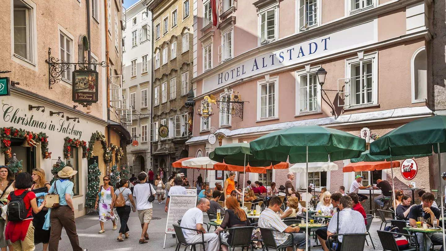 People sit at outdoor dining tables on the pedestrianized street of Salzburg's Old Town
