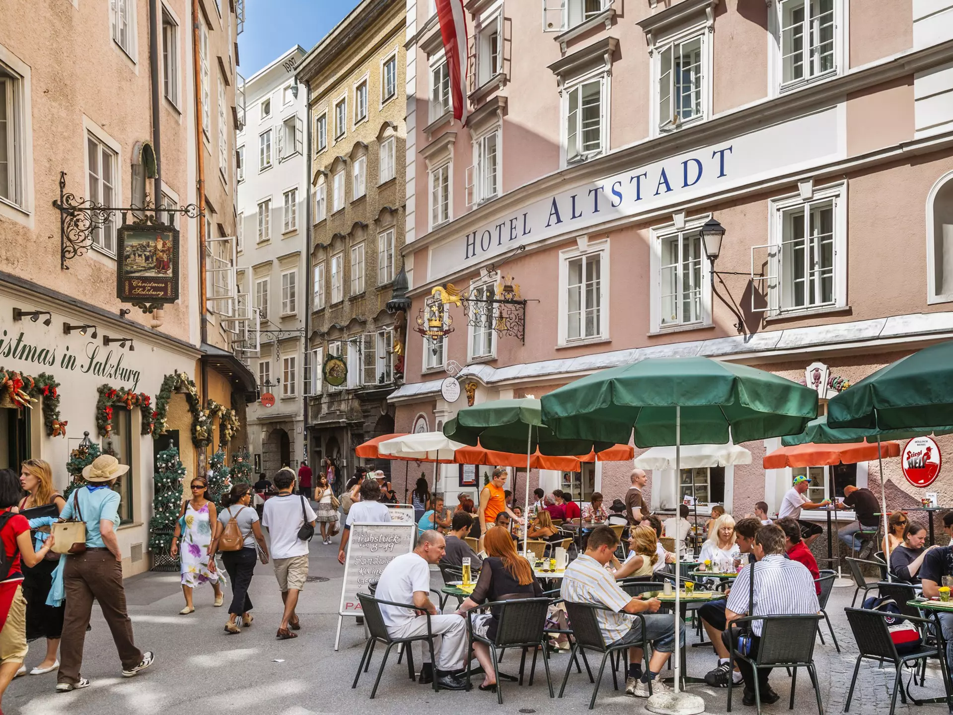 People sit at outdoor dining tables on the pedestrianized street of Salzburg's Old Town