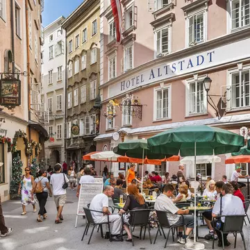 People sit at outdoor dining tables on the pedestrianized street of Salzburg's Old Town