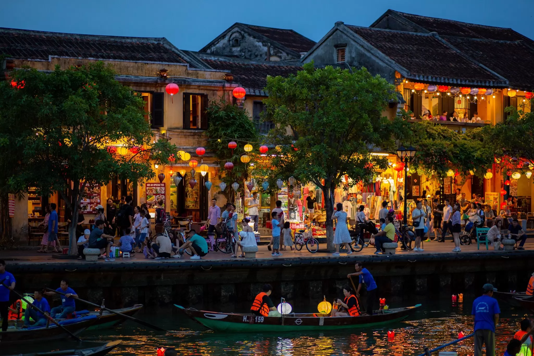 Riverside shops and cafes lit up at night in a busy town.