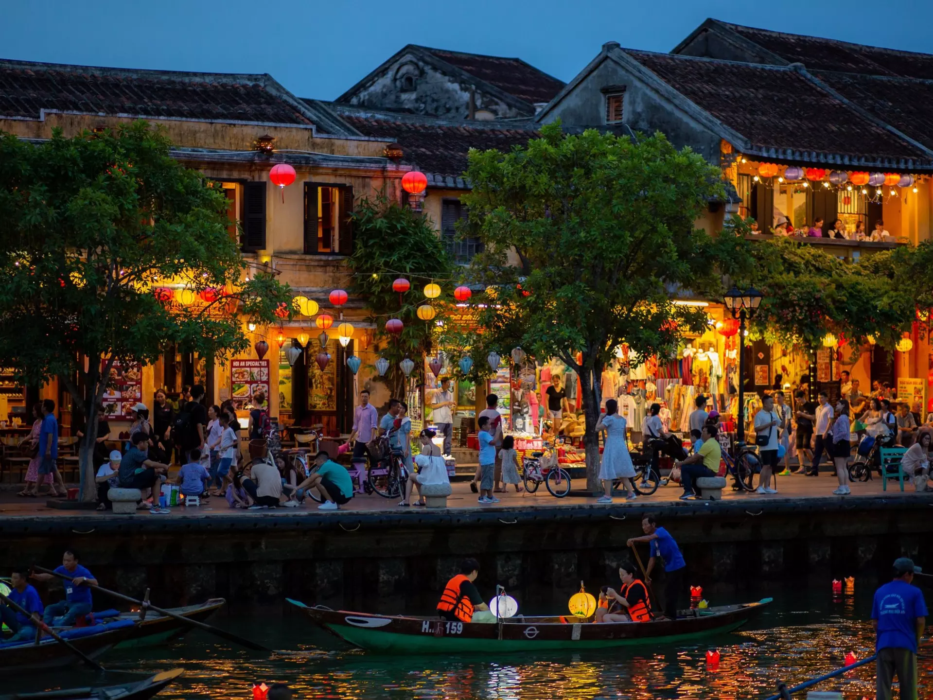 Riverside shops and cafes lit up at night in a busy town.
