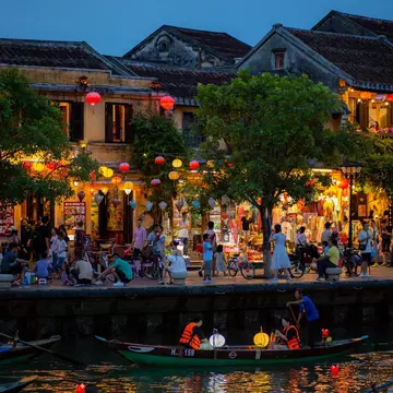Riverside shops and cafes lit up at night in a busy town.