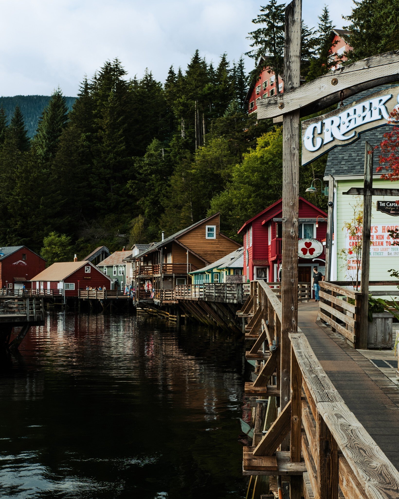 A wooden boardwalk in front of harborfront homes and shops on a sunny day