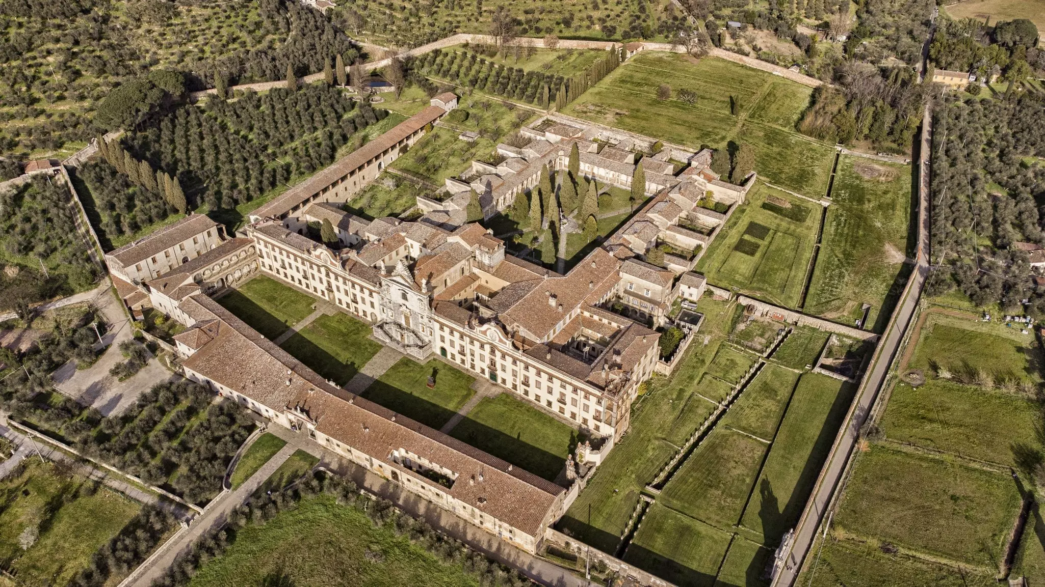 A large monastery complex surrounded by green fields and trees.
