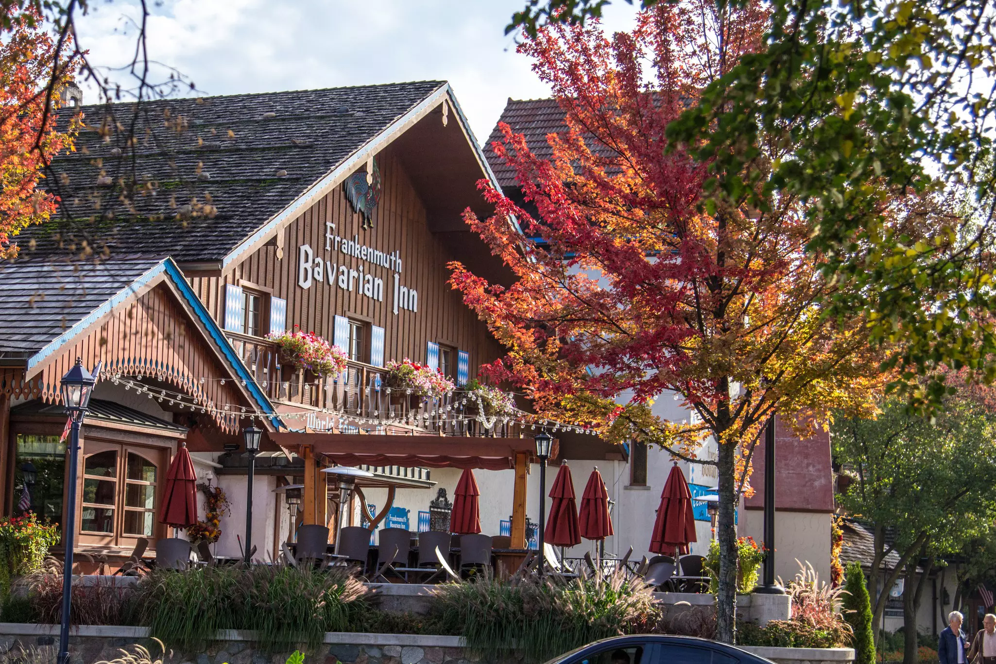 An inn and hotel with a wooden facade in the German style, framed by a tree displaying fall foliage.