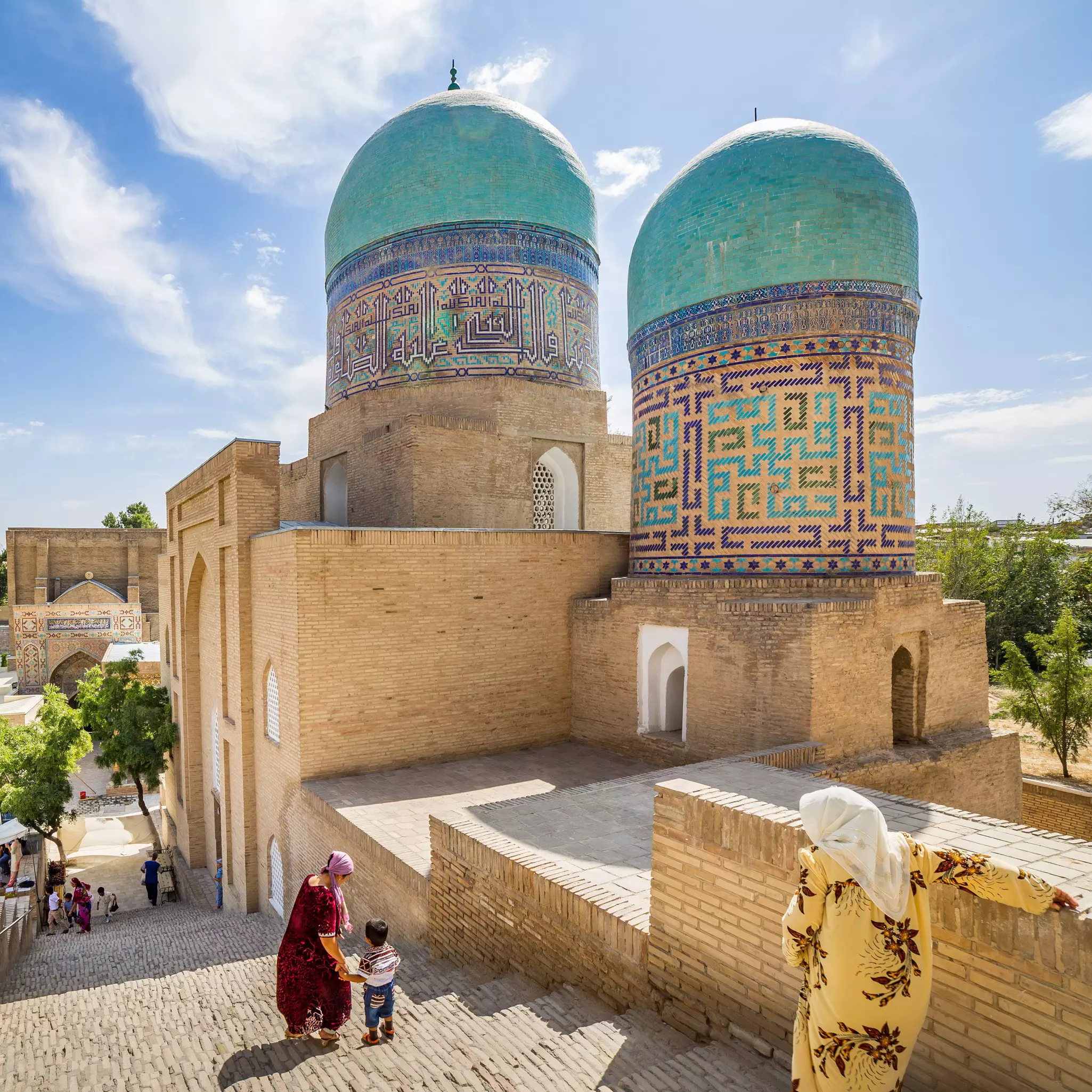 Two women and a child walk past a grand tomb in Shah-i-Zinda, Uzbekistan