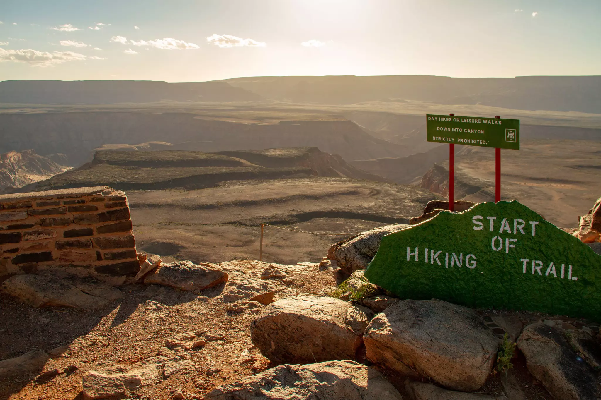 A sign above a vast canyon indicates a trail head. 