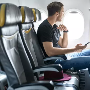 A young male passenger sits in an airplane seat next to the window with a mobile phone