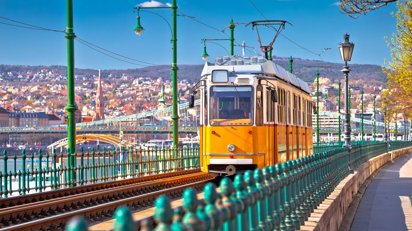 A yellow tram runs along the riverside in Budapest coming toward the camera
