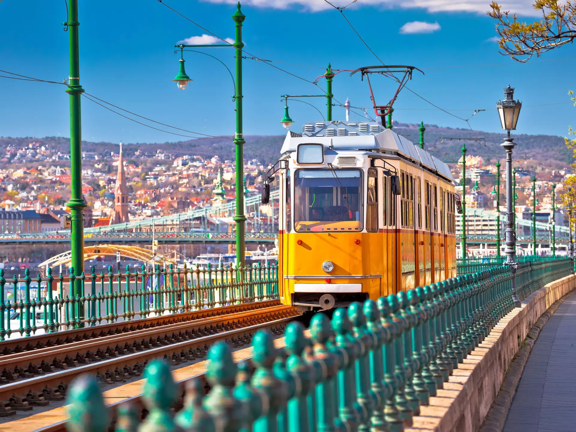 A yellow tram runs along the riverside in Budapest coming toward the camera