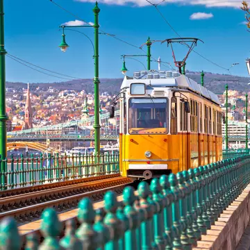 A yellow tram runs along the riverside in Budapest coming toward the camera