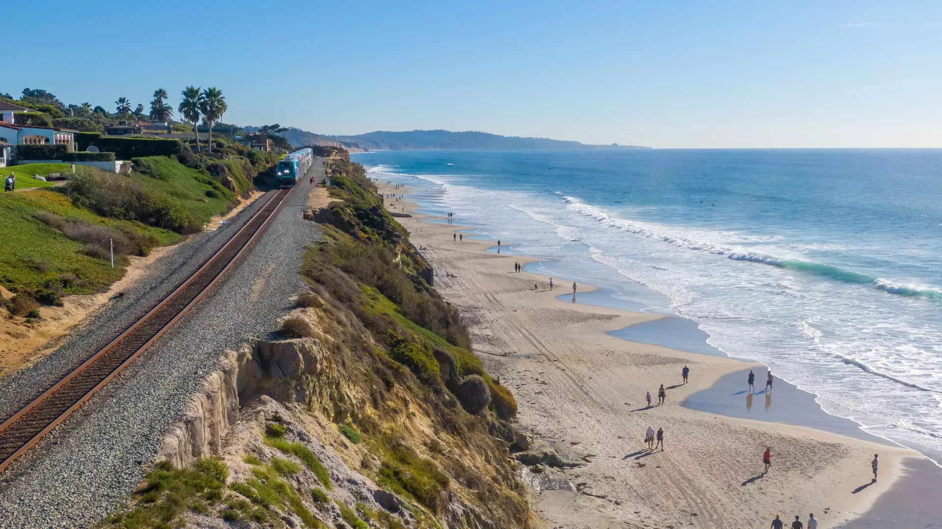 Del Mar, CA, USA - Nov 21, 2022: Daytime Drone Images of the Coaster and Amtrak Trains Hugging The Cliffs Along The Beach in Sunny Del Mar, California: Travel, Transportation, Outdoors