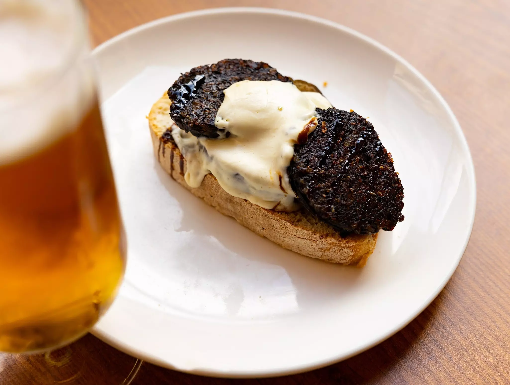 Spanish style sandwich of fresh bread slice topped with morcilla sausage, eggplant, and spicy aioli, complemented by refreshing glass of beer. Typical Salamanca tapas.