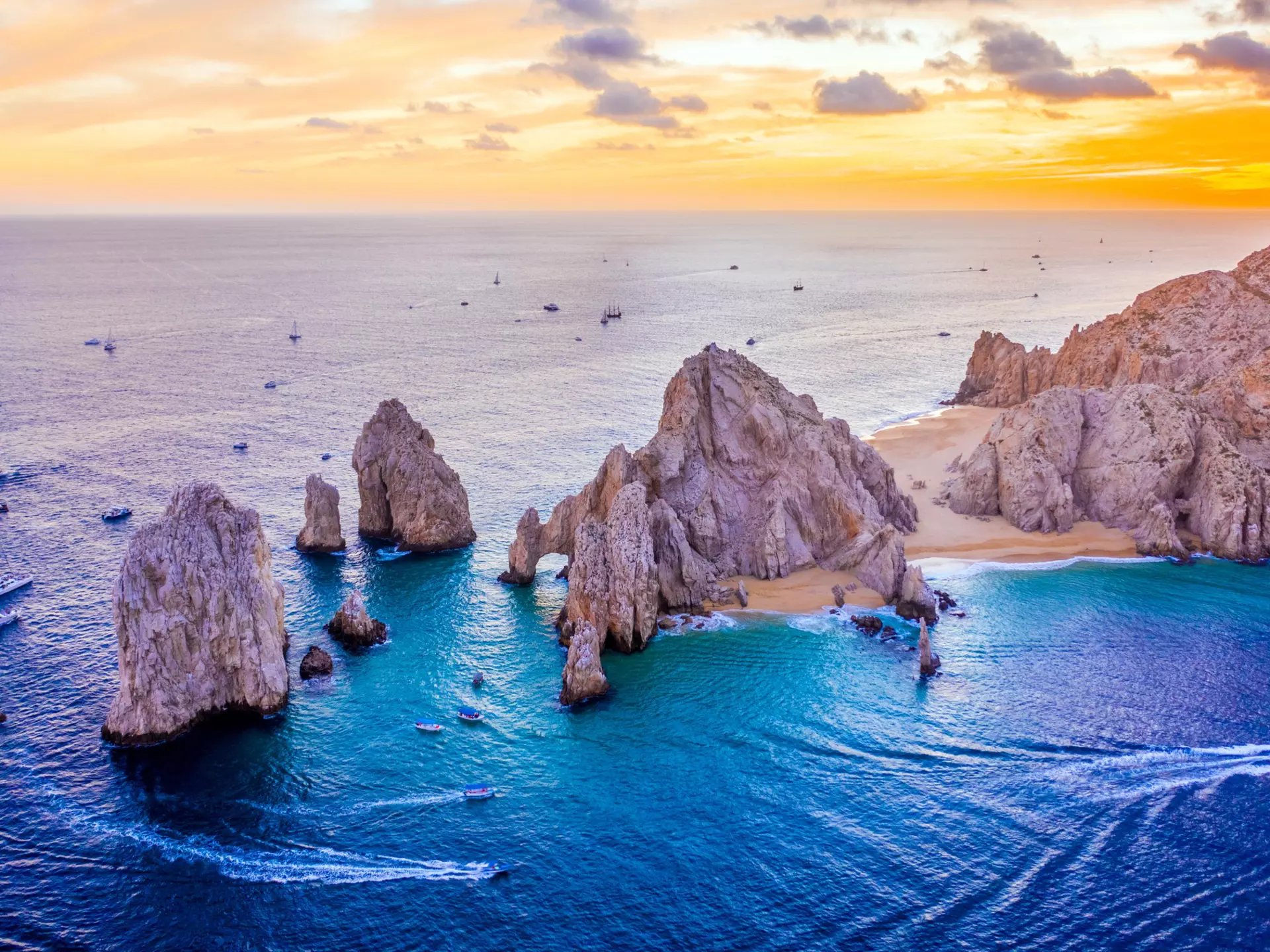 Aerial view of boats speeding by El Arco de Cabo San Lucas, Mexico at sunset