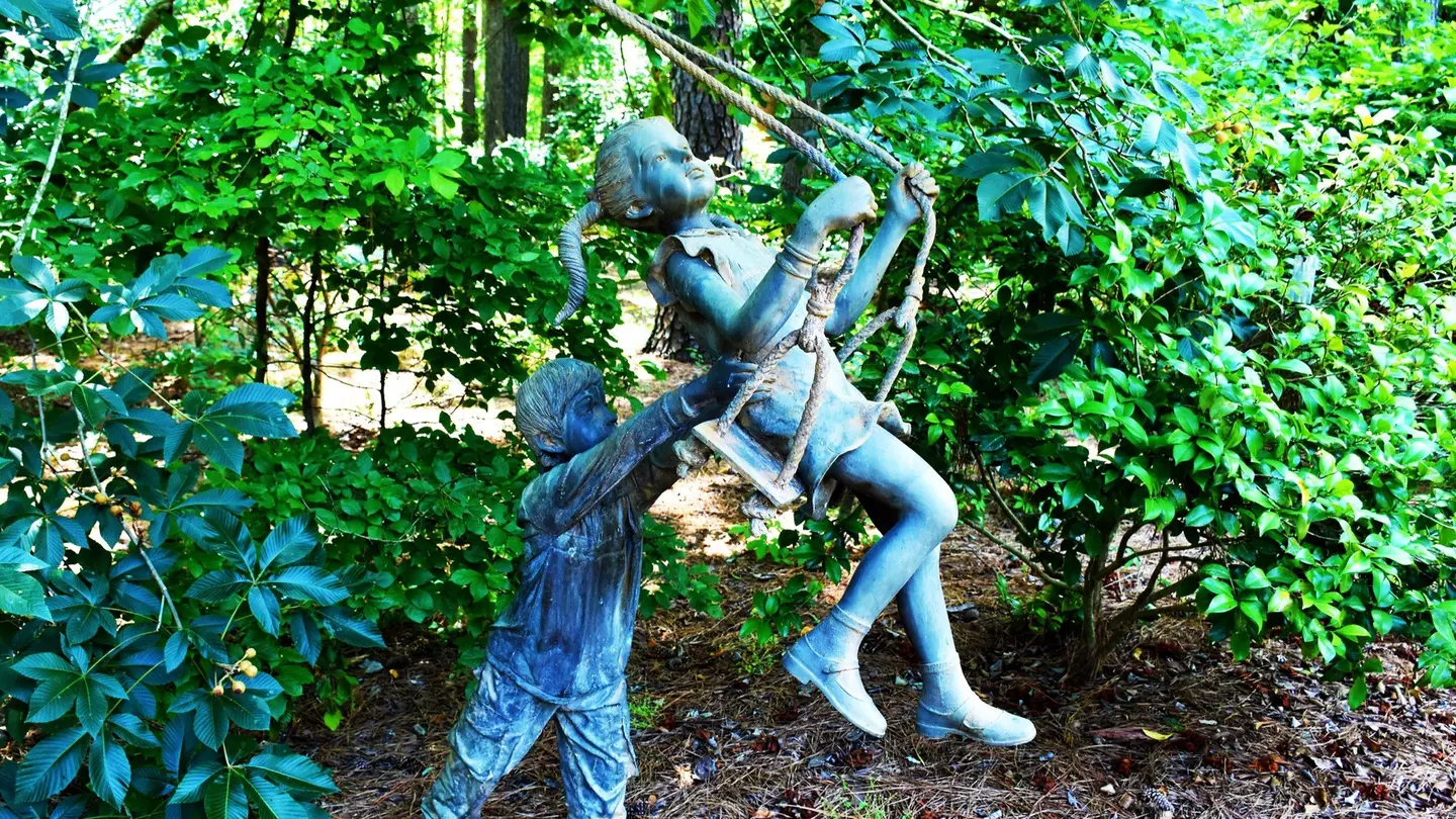 Statue of a young boy pushing a young girl on a swing at the Cape Fear Botanical Garden in Fayetteville, North Carolina.