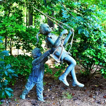 Statue of a young boy pushing a young girl on a swing at the Cape Fear Botanical Garden in Fayetteville, North Carolina.