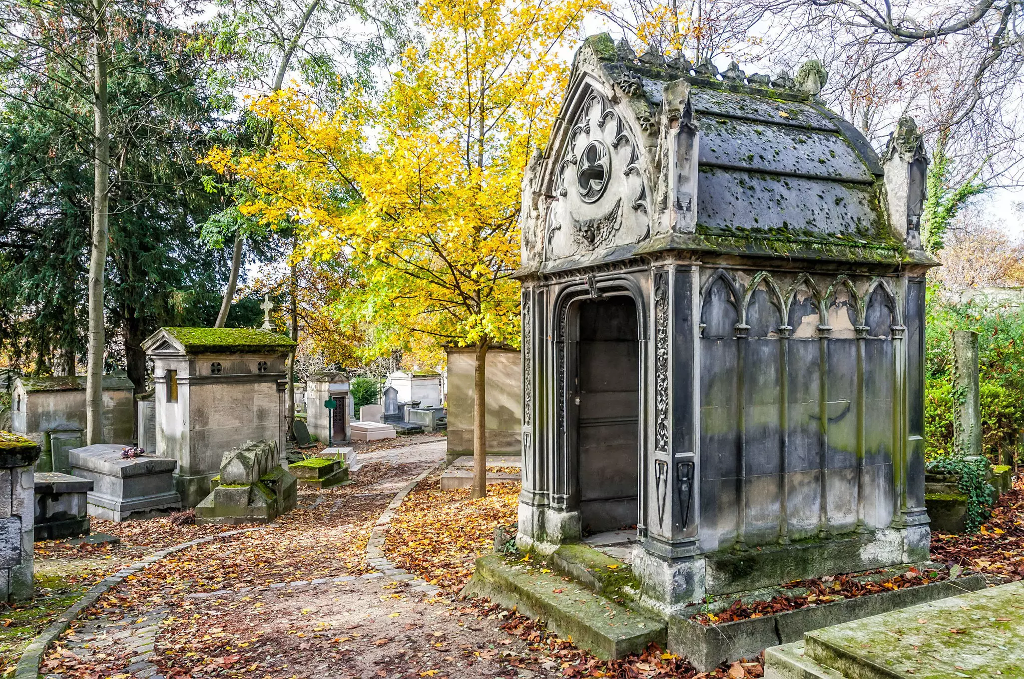 A freestanding stone tomb near a path through a cemetery in Paris.