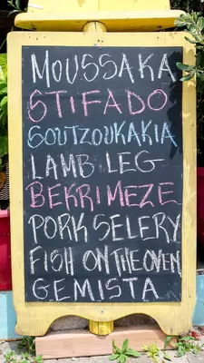 A chalkboard menu listing Greek dishes, including moussaka and stifado.