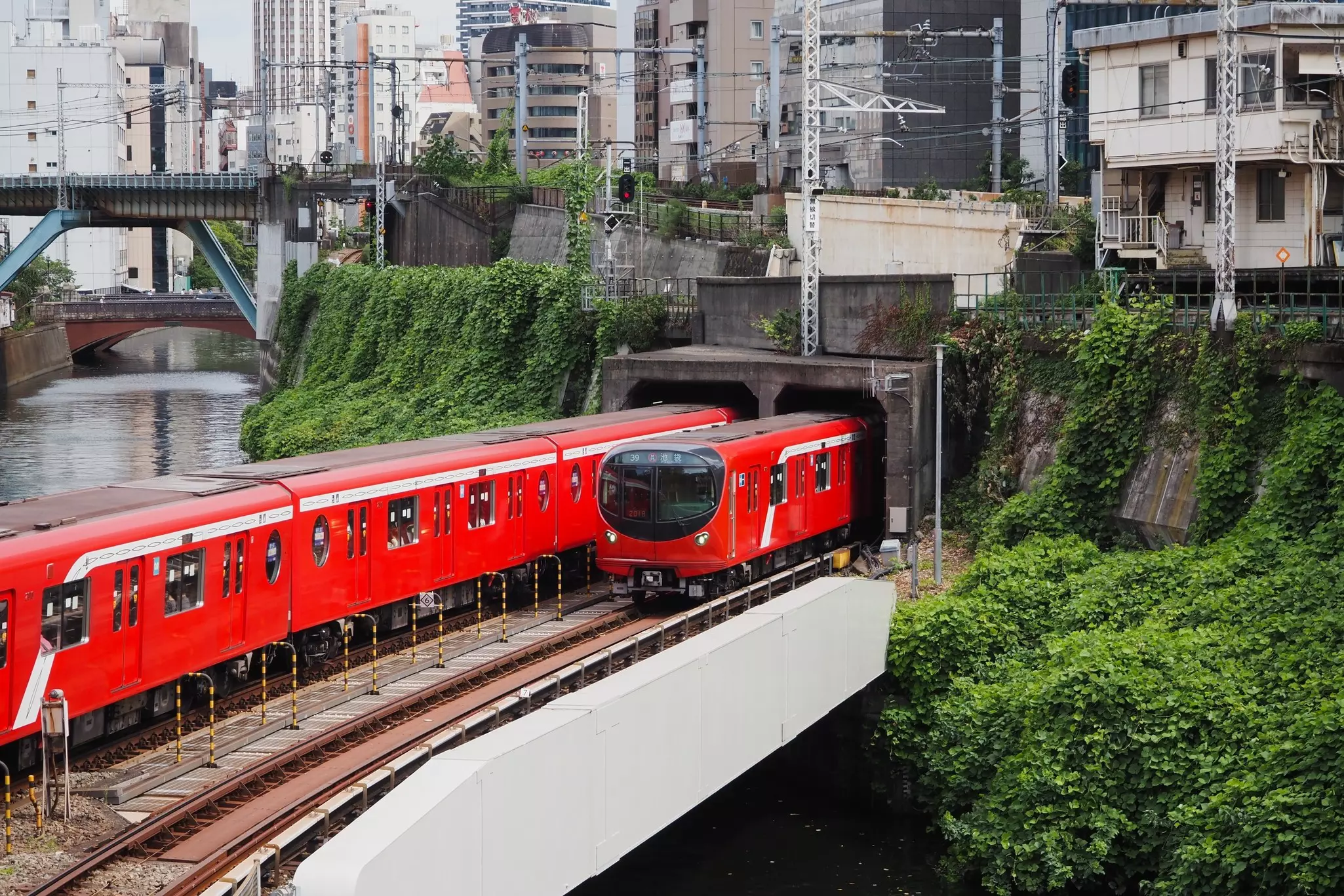 Two red subway trains pass each other as the enter and leave a tunnel in a city.