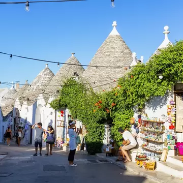 Visitors on a lane of whitewashed trulli with conical stone roofs and souvenir stalls in Alberobello, Puglia, Italy