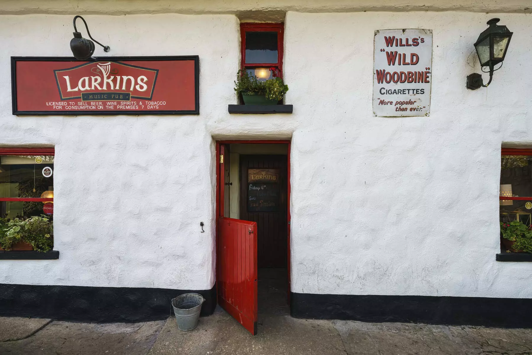The exterior of a pub. The walls are whitewashed and there are two small red-framed timber windows and a red wooden swinging door.