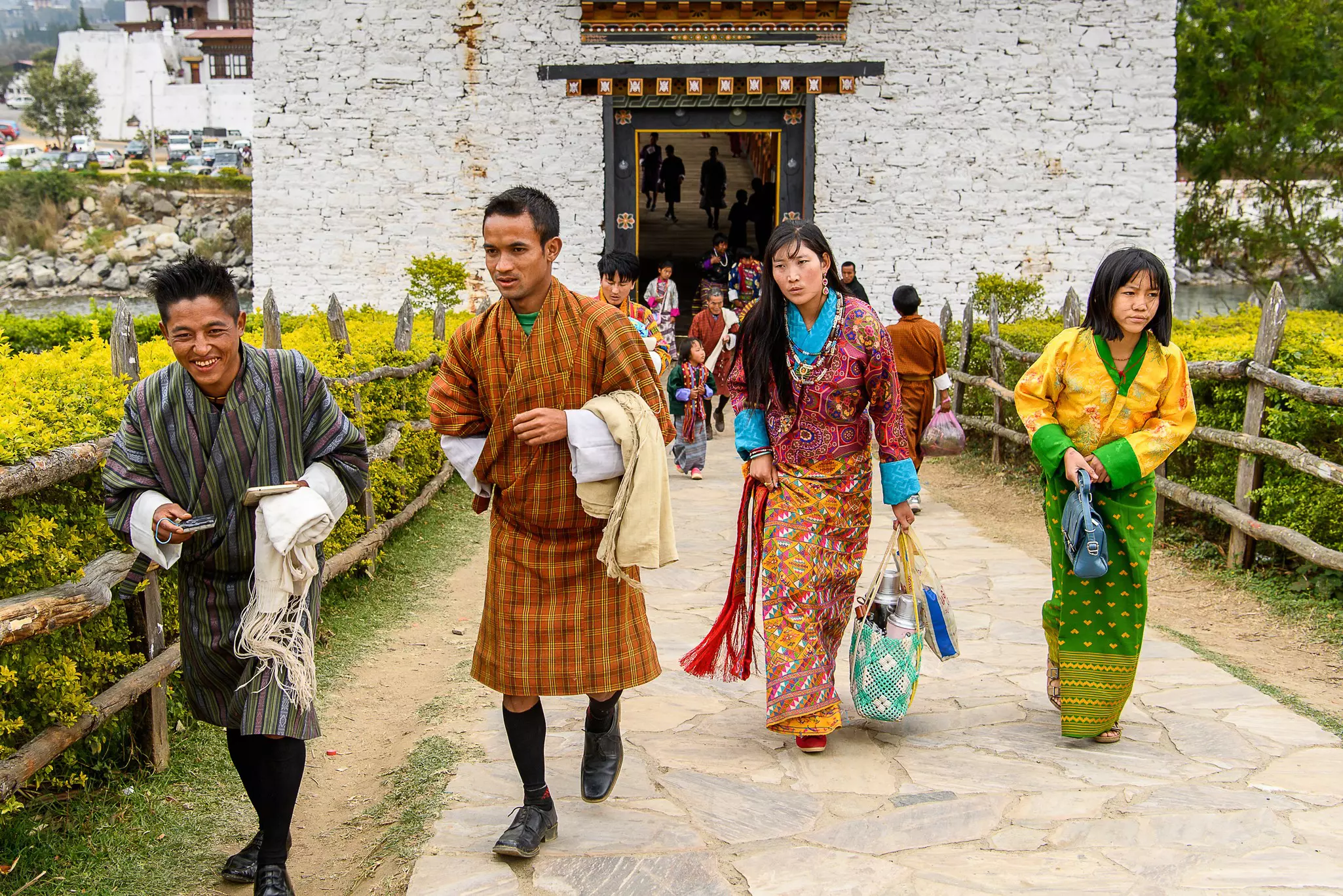 Two women and two men in traditional dress walk down a pathway leading from a white buidling.