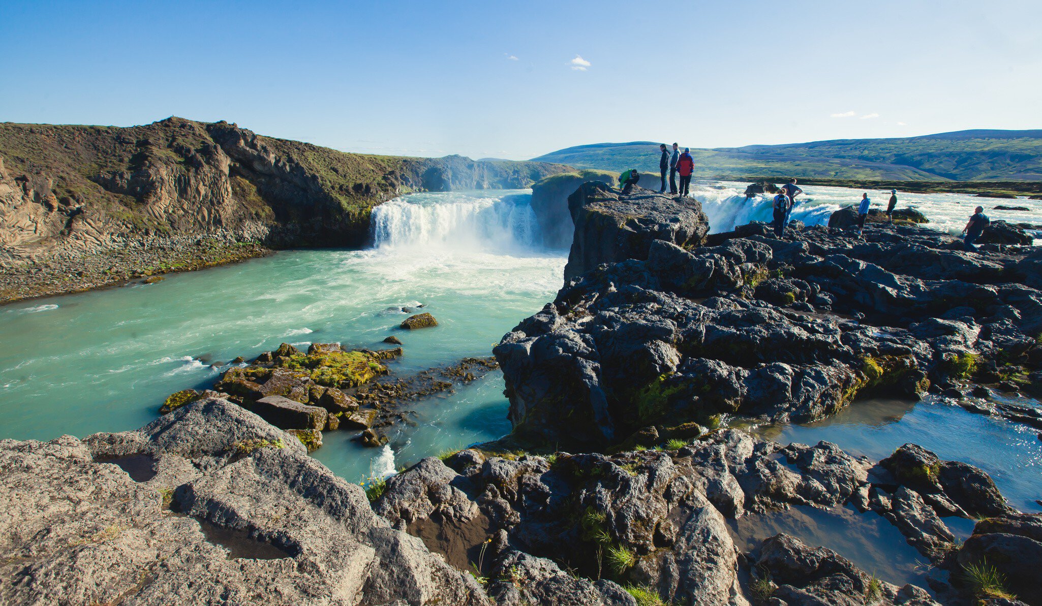 Visitors stand on rocks at the Goðafoss waterfall in Iceland.