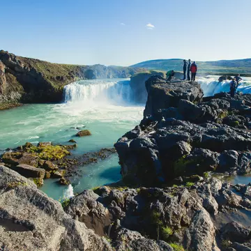 Visitors stand on rocks at the Goðafoss waterfall in Iceland.