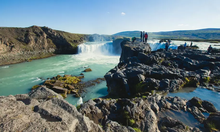 Visitors stand on rocks at the Goðafoss waterfall in Iceland.