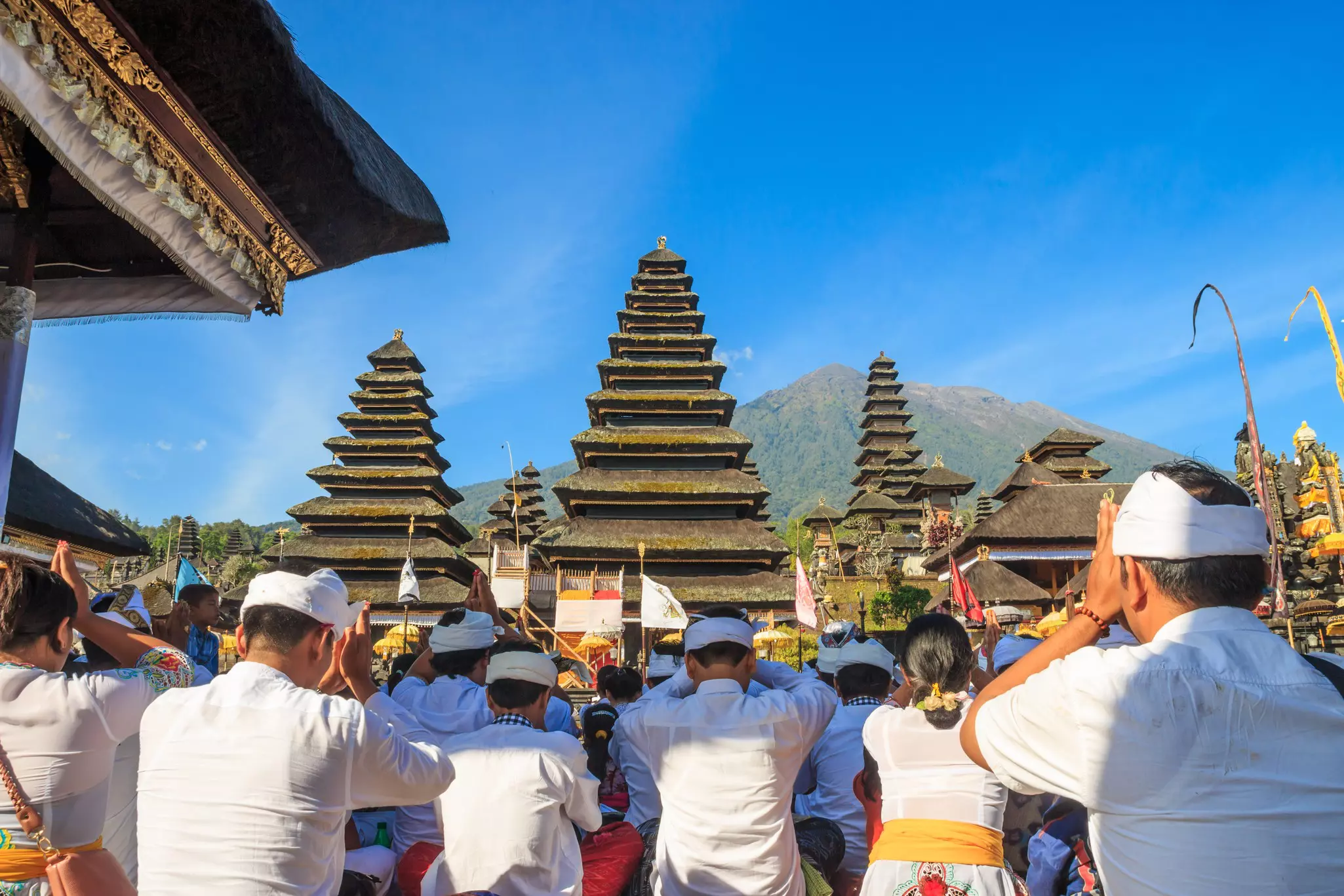 Hindus dressed in white pray in front of the temple spires of Pura Besakih, the largest temple in Bali, Indonesia.