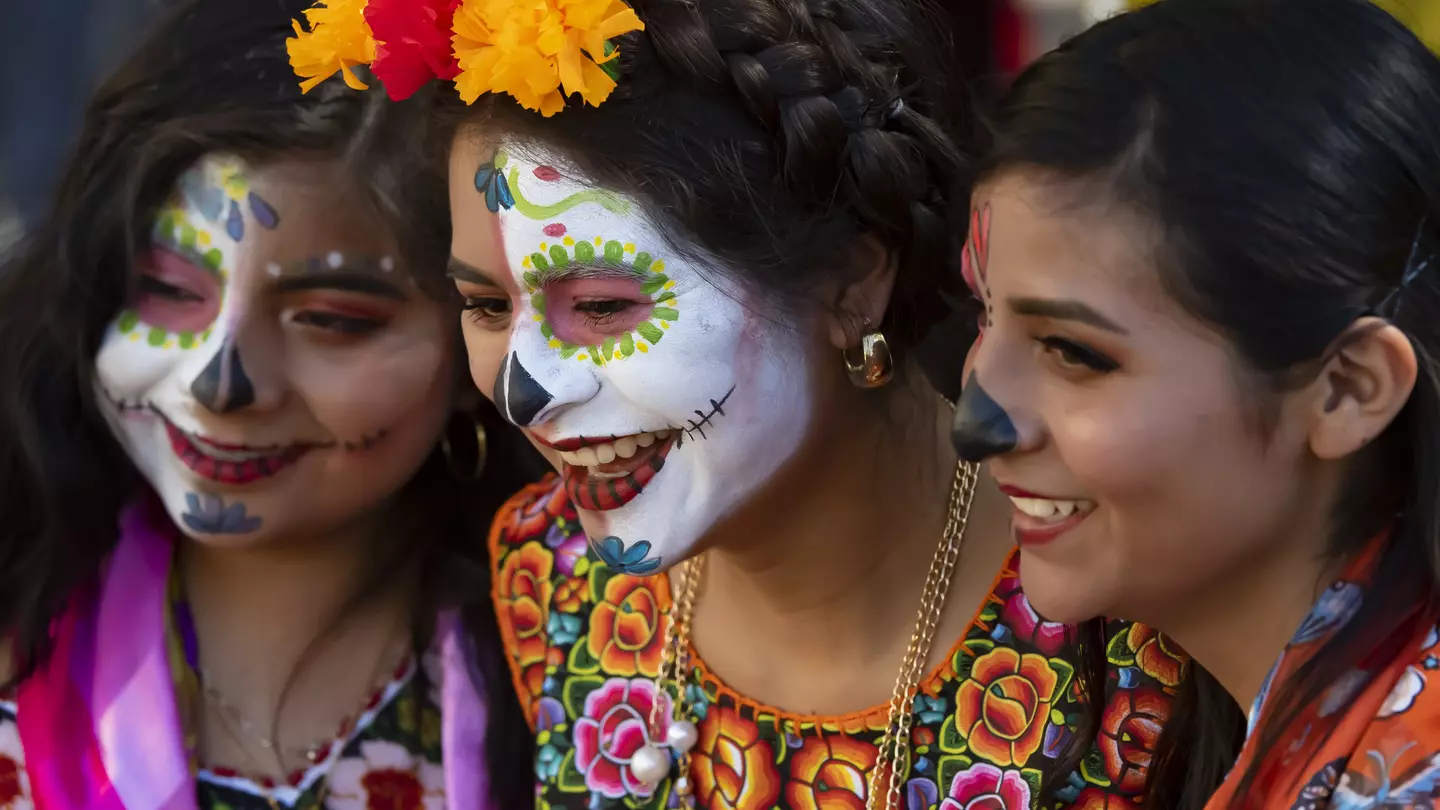 Three girls in traditional outfits, one with skull face paint, at the Dí­a de los Muertos festival in Oaxaca