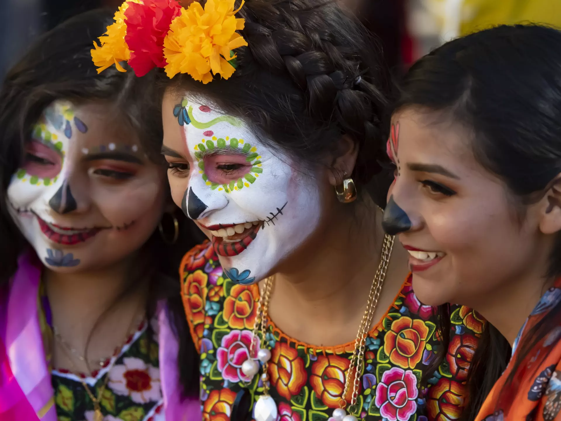 Three girls in traditional outfits, one with skull face paint, at the Dí­a de los Muertos festival in Oaxaca
