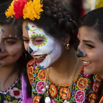 Three girls in traditional outfits, one with skull face paint, at the Dí­a de los Muertos festival in Oaxaca